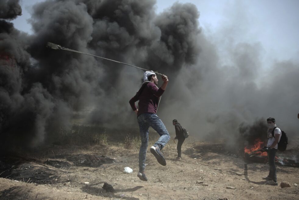 En demonstrant ved Gaza-grensen slynger stein mot israelerne fredag 6. april. Foto: AP / NTB Scanpix