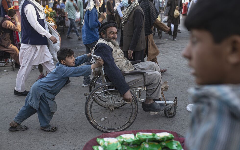En gutt dytter en mann i rullestol gjennom et marked i Kabul.
 Foto: Ahmad Halabisaz / AP / NTB