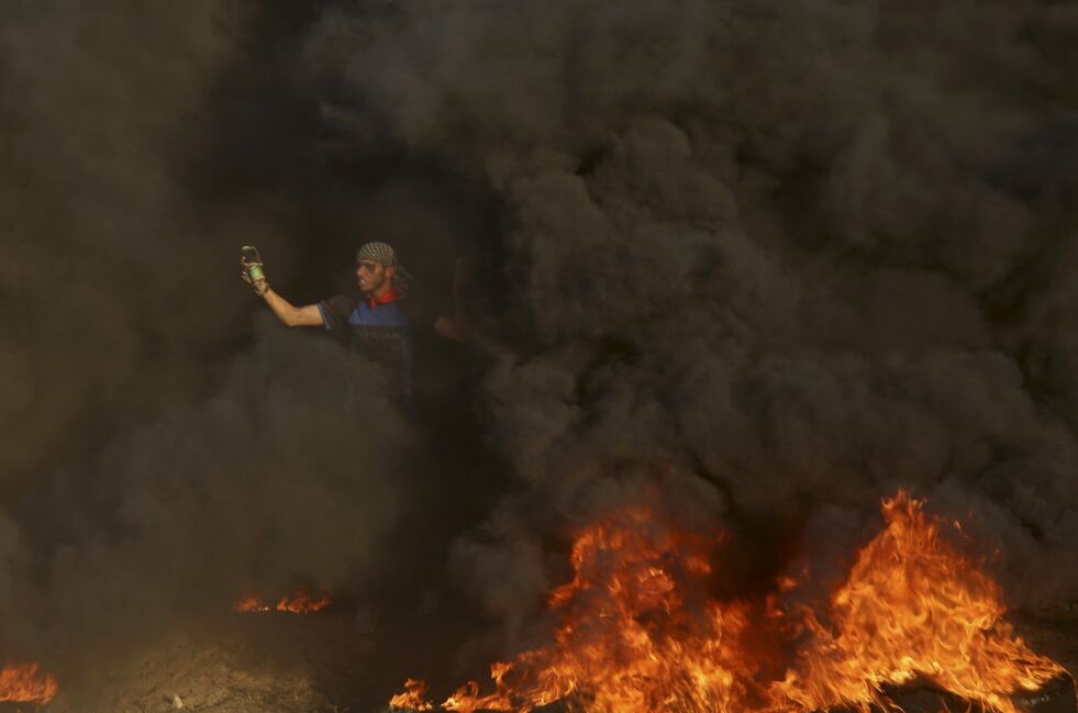 OPPTØYER: En palestinsk demonstrant kaster stein mot israelere ved Gaza-grensen, dekket av røyk fra brennende bildekk. Foto: AP / NTB Scanpix