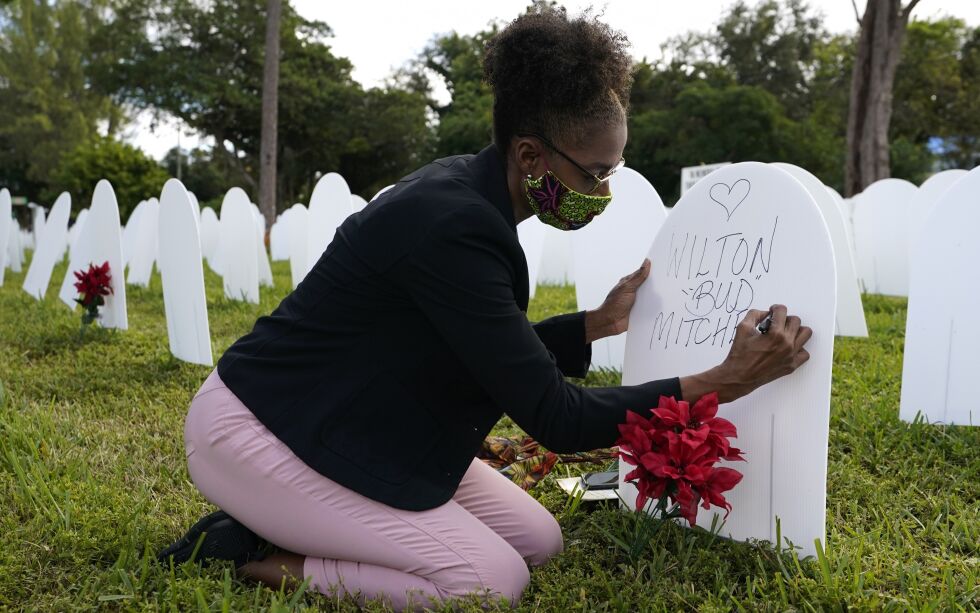 Rachel Moore skriver en hyllest til fetteren Wilton «Bud» Mitchell som døde av COVID-19. Minneplaketten står på en symbolsk kirkegård som ble opprettet i nabolaget Liberty City i Miami for å huske og ære liv som gikk tapt for COVID-19.
 Foto: Lynne Sladky / NTB