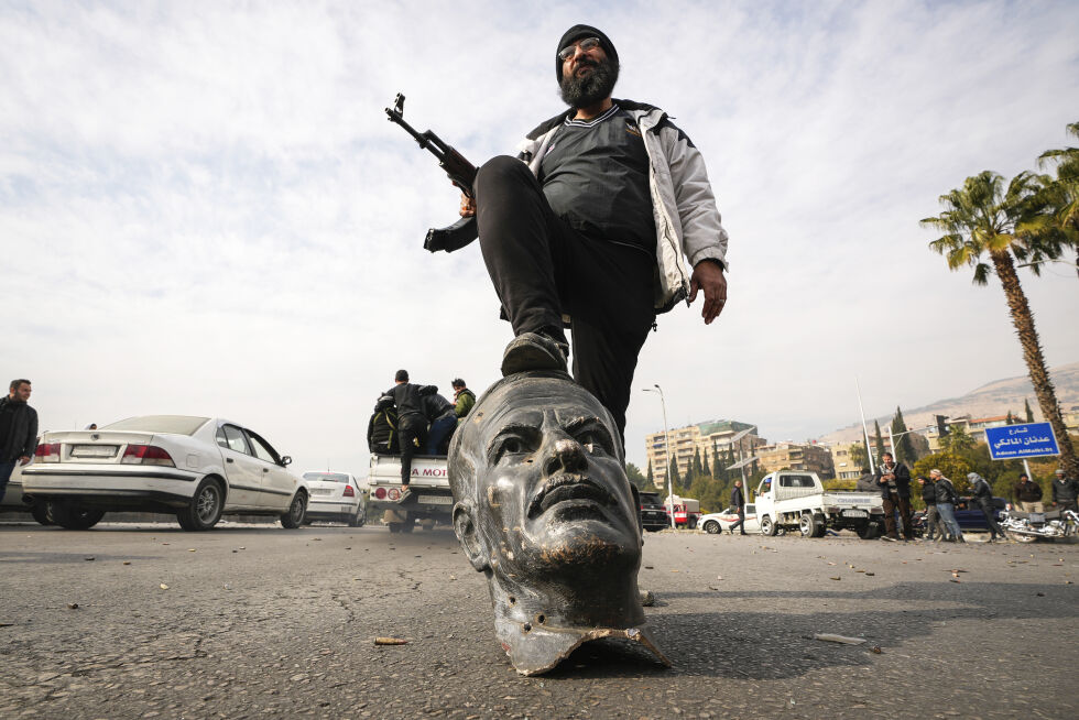 Damaskus: En opposisjonskjemper tråkker på en ødelagt byste av den avdøde syriske presidenten Hafez al-Assad, Bashar al-Assads far, søndag 8. desember 2024.
 Foto: AP Photo/Hussein Malla/NTB