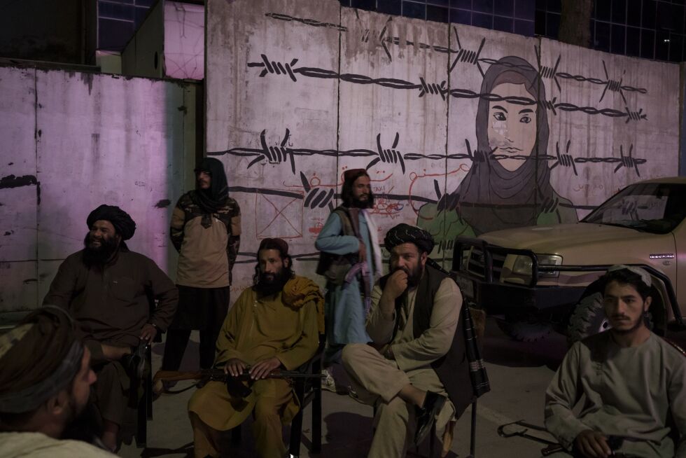 Taliban-medlemmer sitter foran et bilde av en kvinne bak piggtråd i Kabul, Afghanistan.
 Foto: Ap