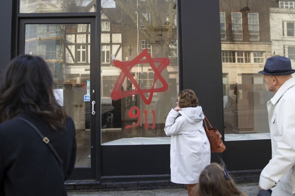 Forbipasserende ser på antisemittisk graffiti på et butikkvindu i Belsize Park i Nord-London, søndag 29. desember 2019. En synagoge og flere butikker i Nord-London har blitt tilgriset av antisemittisk graffiti under den jødiske festivalen i Hanukkah. Det jødiske hellige David-stjernen ved siden av tallene «9.11» ble spraymalt i rødt og lilla på flere lokaler. Graffitien viser til en antisemittisk konspirasjonsteori om at jøder er ansvarlige for terrorangrepet i USA 11. september 2001 hvor 2.996 mennesker ble drept.
 Foto: Aaron Chown/NTB Scanpix