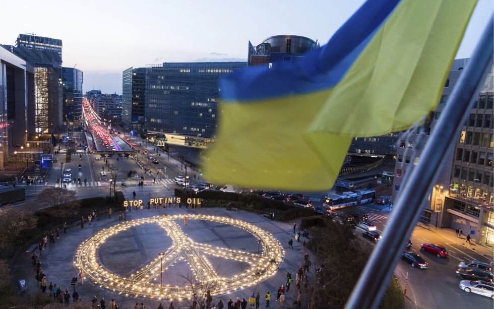 Et ukrainsk flagg blafrer i vinden mens et gigantisk fredsskilt av levende lys settes opp av demonstranter i forkant av et EU- og NATO-toppmøte i Brussel, tirsdag 22. mars 2022. Demonstranter ba EU-ledere om å innføre et fullstendig forbud mot russisk drivstoff og å holde ett minutts stillhet for å hedre krigens ofre. Illustrasjonsbilde.
 Foto: Geert Vanden Wijngaert/AP/NTB